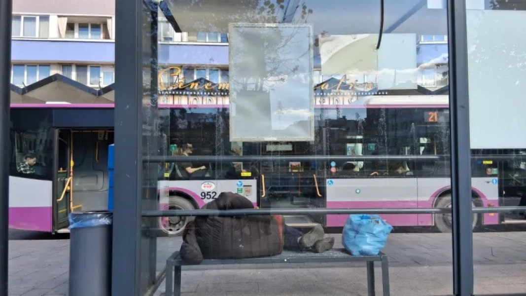 Un om al străzii îngheață pe o bancă în stația de autobuz din Piața Mihai Viteazu